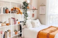 a lovely teen room with a black bed, a large open storage shelf with blooms and pumpkins, a shelf and a mirror over the bed