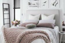 a neutral and pastel bedroom with a grey upholstered bed, layered blankets, black touches and bulbs hanging down