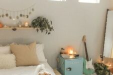 a neutral teen bedroom with neutral walls, a pallet bed, a floor mirror, a blue storage cabinet, a floating shelf with greenery and candles and a guitar