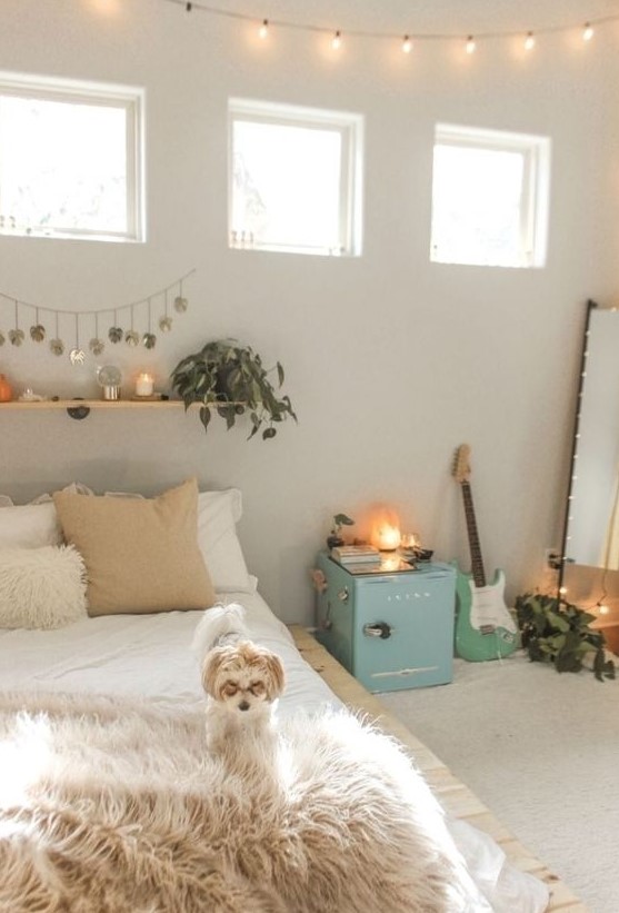 a neutral teen bedroom with neutral walls, a pallet bed, a floor mirror, a blue storage cabinet, a floating shelf with greenery and candles and a guitar