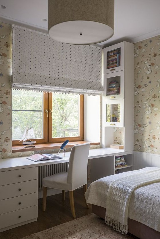 a neutral teen room with printed map wallpaper, a built-in desk with storage units, a bed with neutral bedding and a curtain