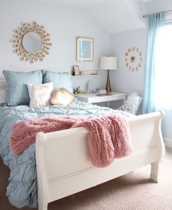 a pastel bedroom with a white bed and pastel bedding, blue curtains, a white desk as a nightstand, a white chair, a clock, a mirror and a table lamp