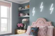 a pastel teen bedroom with blue walls, a pink bed with pastel bedding, built-in shelves, a stained dresser and blush curtains