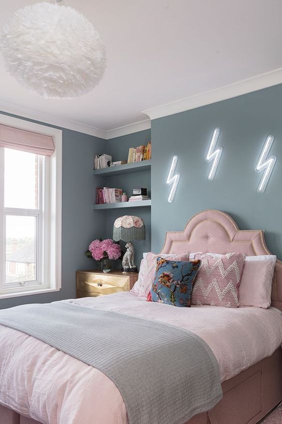 a pastel teen bedroom with blue walls, a pink bed with pastel bedding, built in shelves, a stained dresser and blush curtains