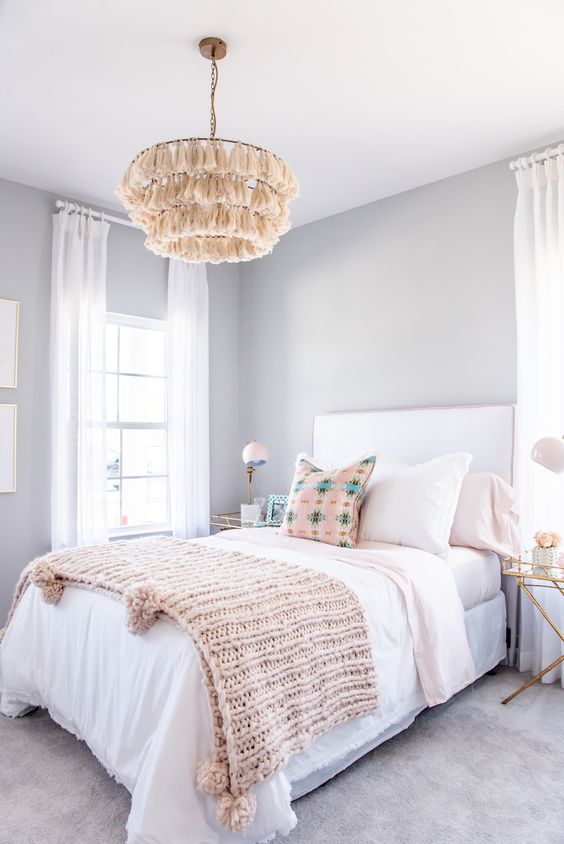 a pretty and relaxed teen girl bedroom with light grey walls, a white bed with pastel bedding, nightstands and tassel chandeliers