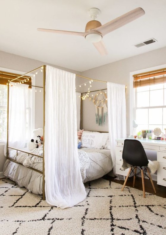 a welcoming modern teen girl bedroom with a brass canopy bed with lights, some boho decor and various textiles for styling the room