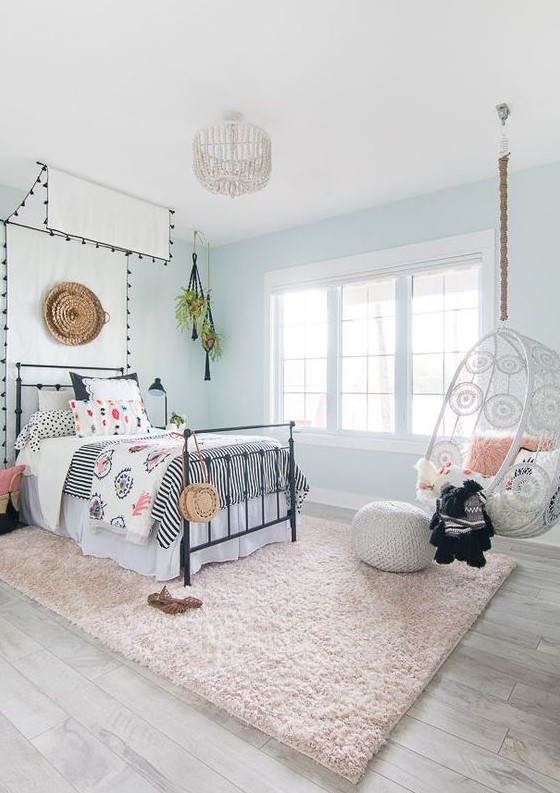 an airy boho teen girl bedroom with light blue walls, a bed with a cnaopy, printed bedding, a suspended chair and a blush rug