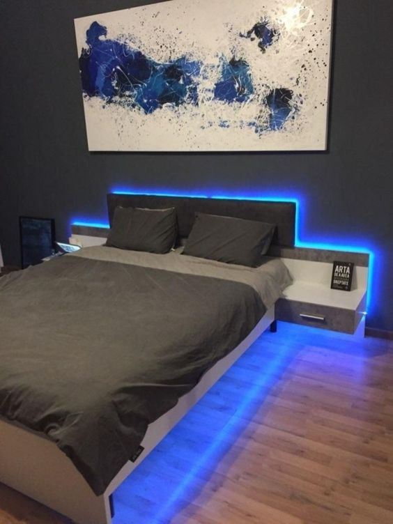 a bold grey and blue teenage bedorom with blue neon lights, a white double bed and a bold artwork