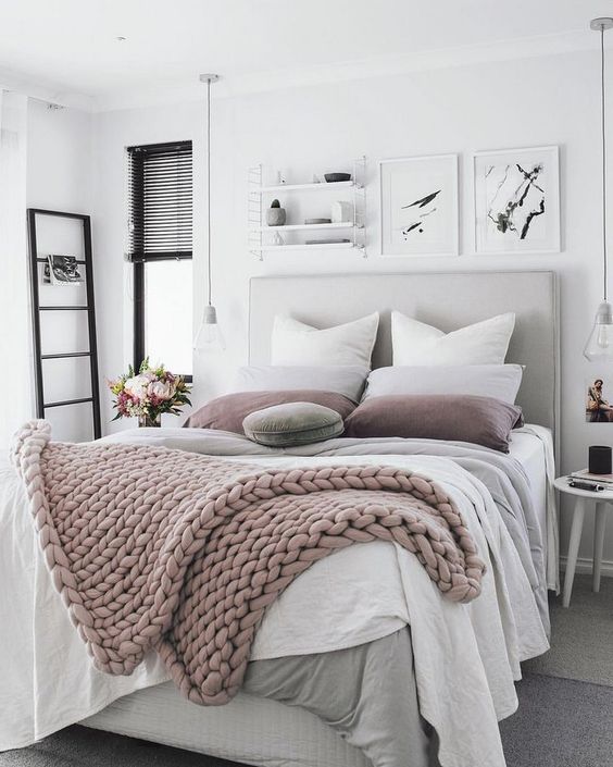 a neutral and pastel bedroom with a grey upholstered bed, layered blankets, black touches and bulbs hanging down