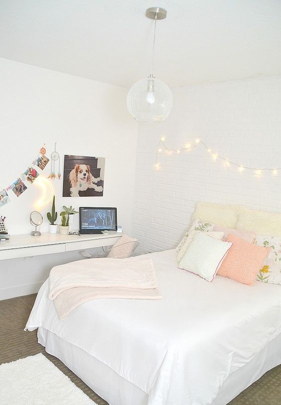 a neutral teen bedroom with a floating desk and vanity, a bed with pastel pillows and lights on the wall