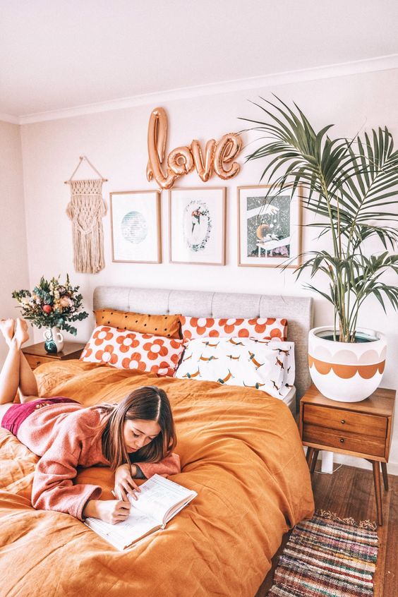a boho girl's bedroom with a grey upholstered bed, bright bedding, stained nightstands, a potted plant and a cool gallery wall