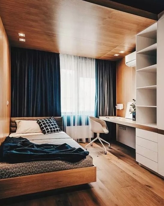 a bold minimalist teen room with a wooden ceiling with lights, navy curtains, a storage unit with a built-in desk, a comfy bed and blue bedding