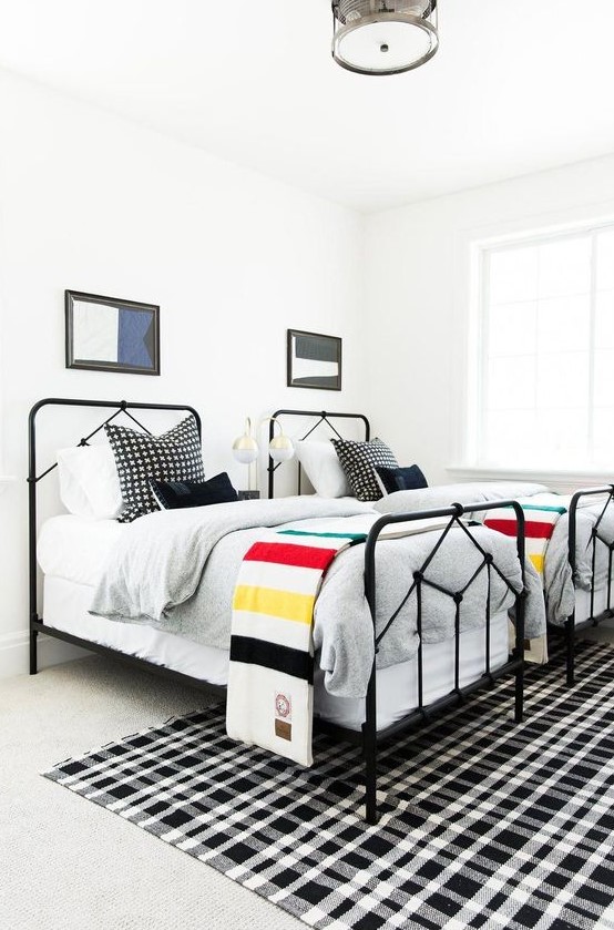 a bright shared boy bedroom with white walls, black beds, layered rugs and bright graphic bedding