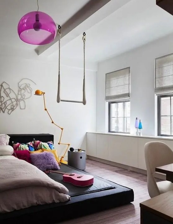 a bright teen girl bedroom with a black platform bed, a hot pink pendant lamp, colorful bedding, simple shades is welcoming