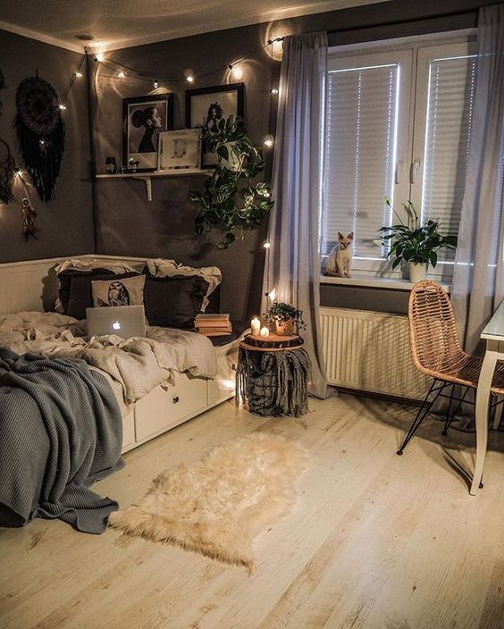 a catchy boho teen bedroom with grey walls, a white bed, stools, a desk and a rattan chair, string lights and greenery