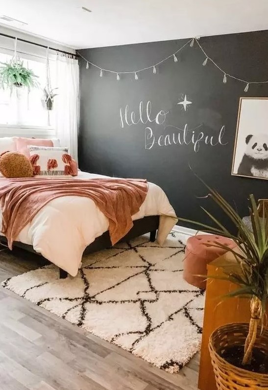 a chic teen bedroom with a chalkboard wall, a bed with pretty pink bedding, a wooden desk, a chair and a footrest