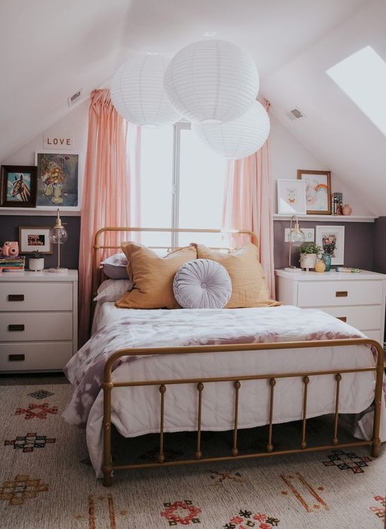 a cozy modern teen bedroom with a brass bed with bedding, white nightstands, lamps and some art plus a printed rug