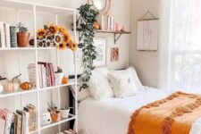 a lovely teen room with a black bed, a large open storage shelf with blooms and pumpkins, a shelf and a mirror over the bed