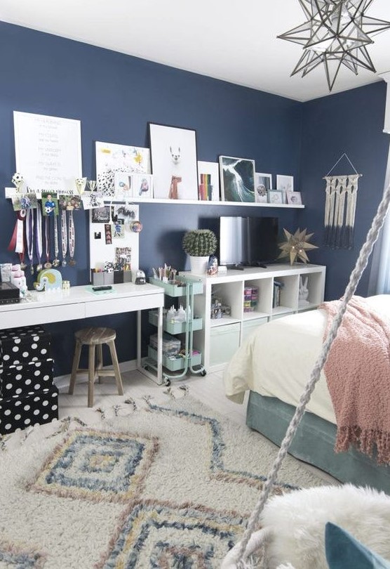 a lovely teen room with navy walls, a turquoise bed, neutral and pastel bedding, a white desk or makeup vanity, a storage unit and a ledge gallery wlal