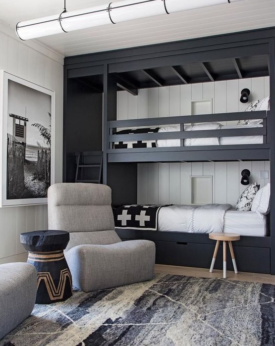 a monochromatic shared boy bedroom with black bunk beds, drawers, grey chairs and a graphic rug