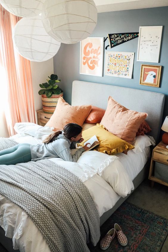 a muted color bedroom with a blue accent wall, a grey upholstered bed with muted color pillows, a gallery wall, nightstands and pendant lamps