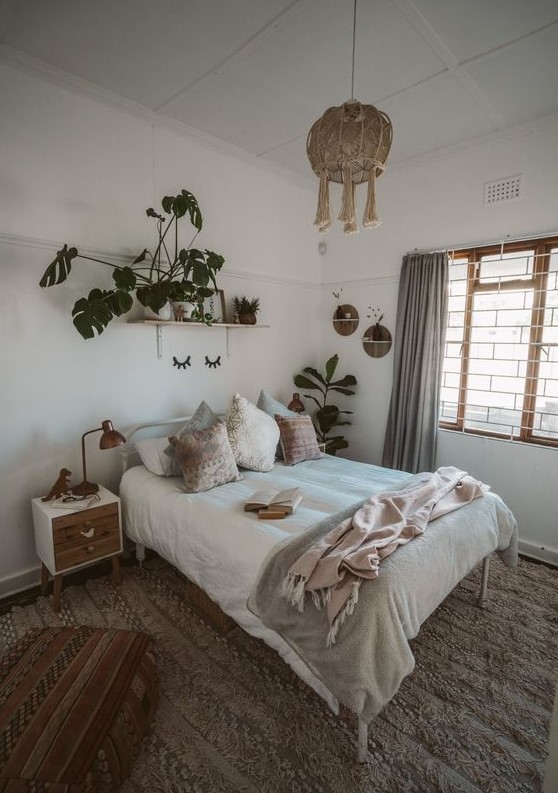 a neutral boho bedroom with a white forged bed with neutral bedding, nightstands, grey curtains, potted plants and a woven pendant lamp