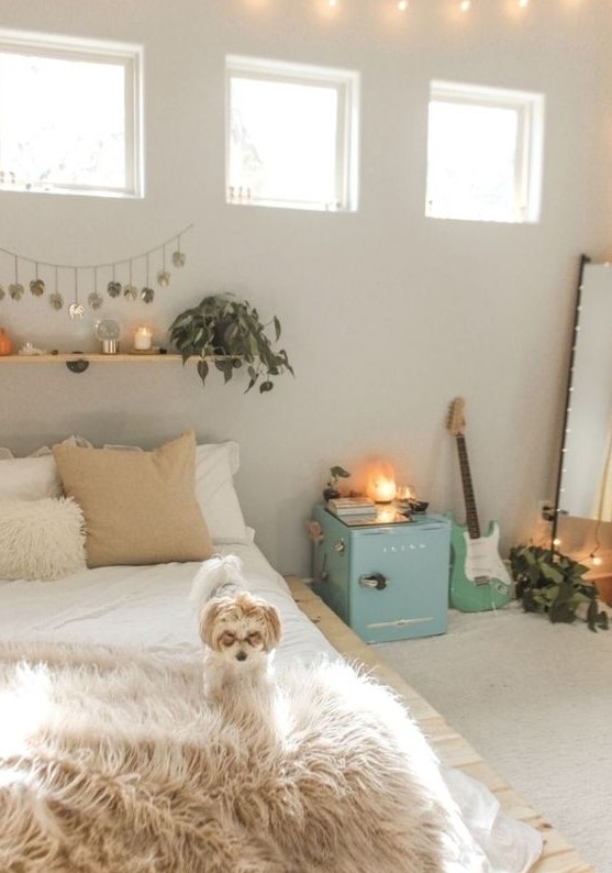 a neutral teen bedroom with neutral walls, a pallet bed, a floor mirror, a blue storage cabinet, a floating shelf with greenery and candles and a guitar