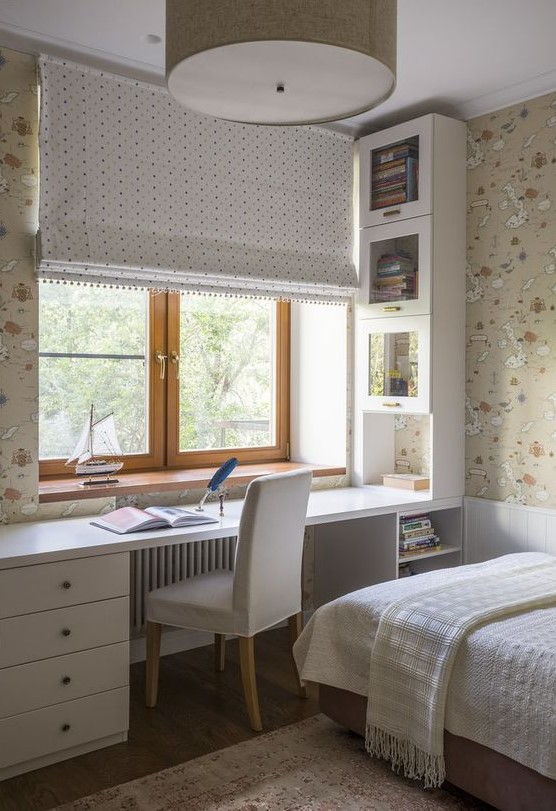 a neutral teen room with printed map wallpaper, a built-in desk with storage units, a bed with neutral bedding and a curtain