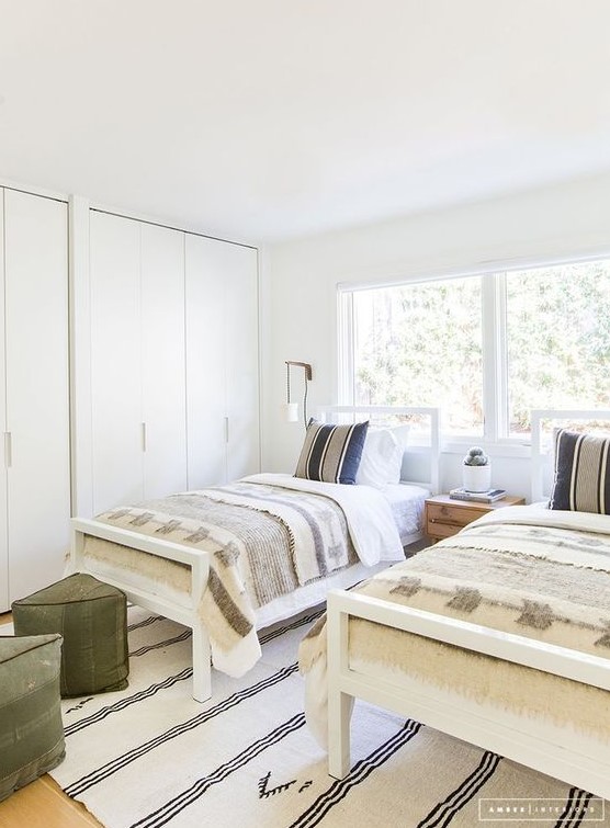 a serene shared boy bedroom in neutrals, with two beds, green ottomans and a large storage unit