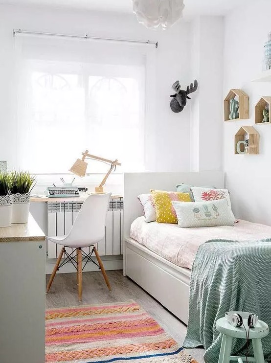 a small pastel teen bedroom with a white desk and a white bed, pastel bedding, a chair and a windowsill for storage, a bright rug