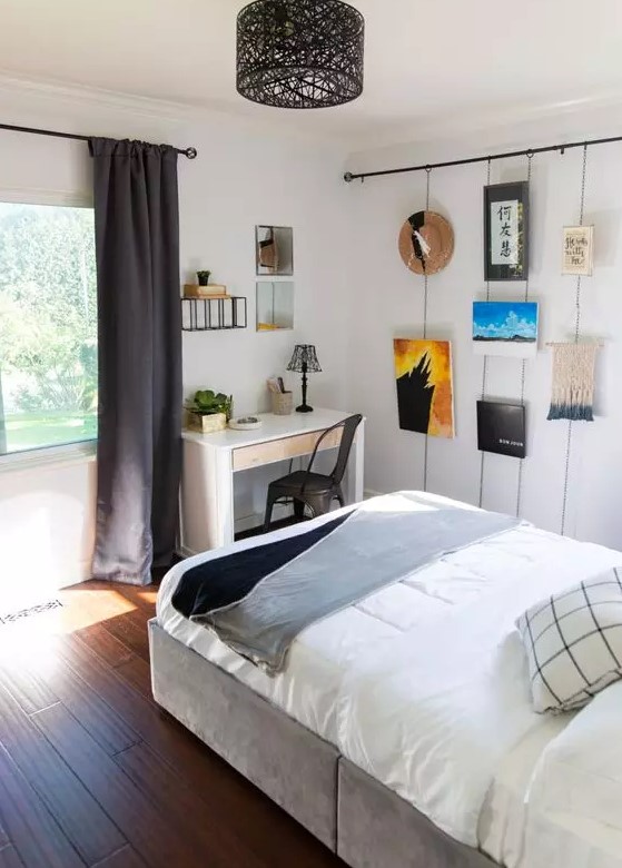 a small teen bedroom with a grey bed with neutral bedding, a white desk and a black chair, a gallery wall and dark curtains
