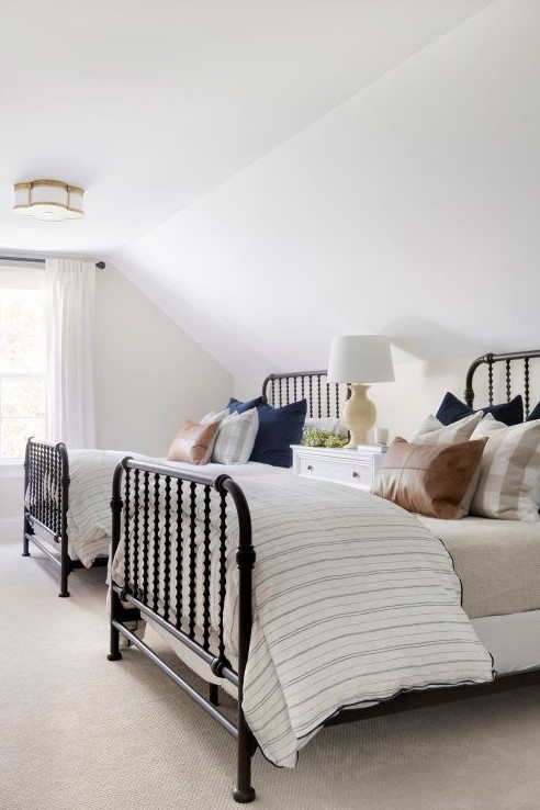 a stylish traditional attic shared bedroom with metal beds, a sideboard as a nightstand, printed bedding