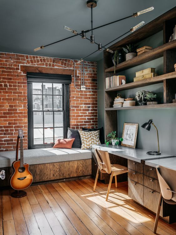 a teen bedroom with a brick accent wall, grey walls, windowsill bed, stained shelves, a long desk, a cool chandelier