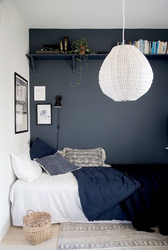 a teen bedroom with a graphite grey wall, an open shelf, a bed with navy bedding, a basket, a pendant lamp and a rug