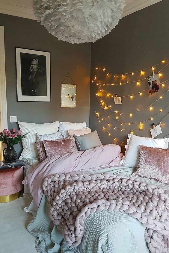 a teen bedroom with grey walls, a bed with grey and pink, string lights on the wall, a fluffy pendant lamp and blooms