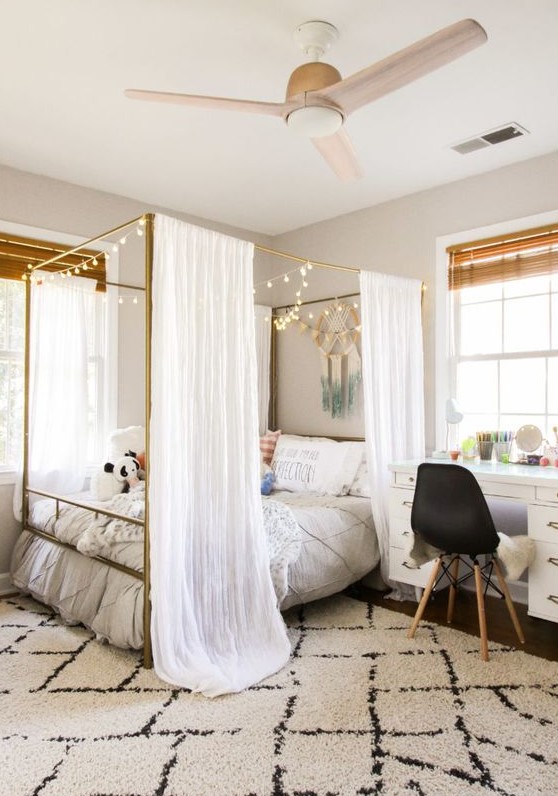 a welcoming modern teen girl bedroom with a brass canopy bed with lights, some boho decor and various textiles for styling the room