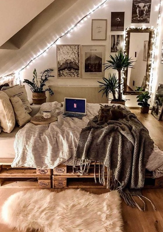 an attic teen room with a pallet bed with pretty bedding, a black and white gallery wall, a mirror and lots of lights and potted greenery