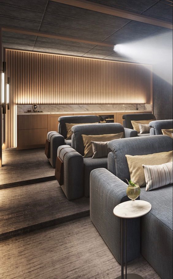a chic contemporary home theater with a light stained bar, built in lights and grey seating furniture and neutral pillows