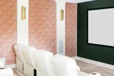 a chic home theater with retro vibes, with pink upholstered walls for better sound, gold sconces, white chairs and a large screen is wow