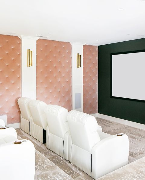 a chic home theater with retro vibes, with pink upholstered walls for better sound, gold sconces, white chairs and a large screen is wow