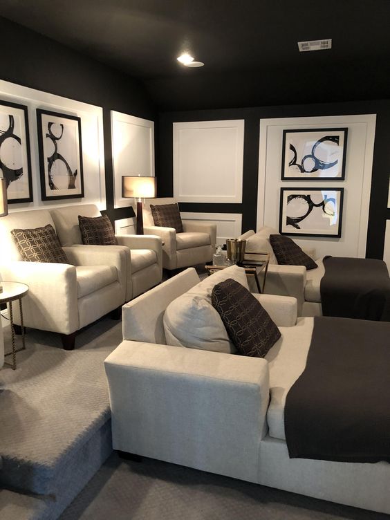 a comfortable and stylish home theater with black walls and a ceiling, neutral seating furniture, dark brown textiles and floor lamps