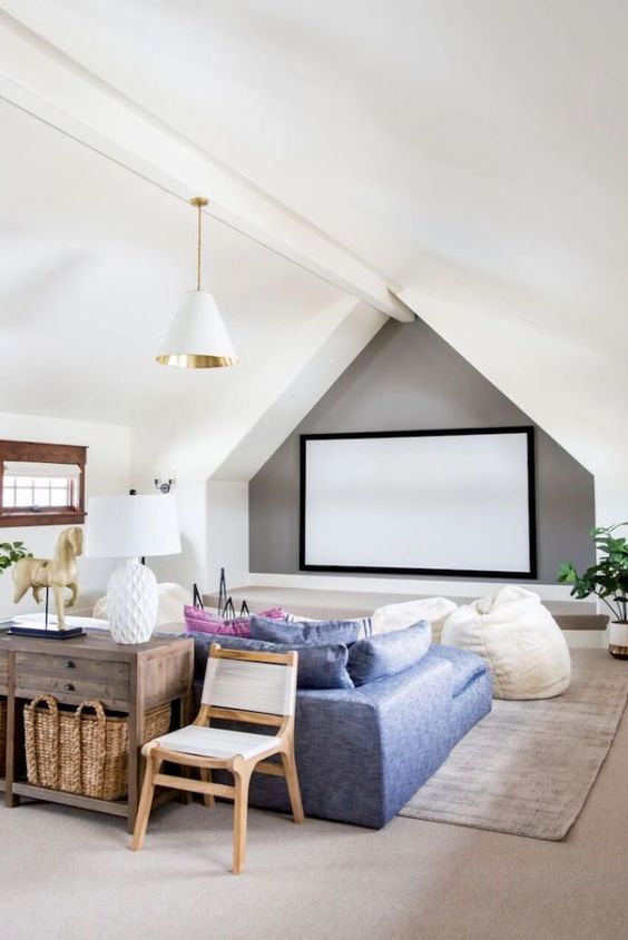 a cool attic home theater with a large screen, a blue sofa and creamy beanbag chairs, a stained console table and neutral chairs