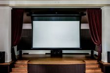a luxurious and chic home theater with stained walls and leather seating furniture, burgundy velvet curtains and chair covers