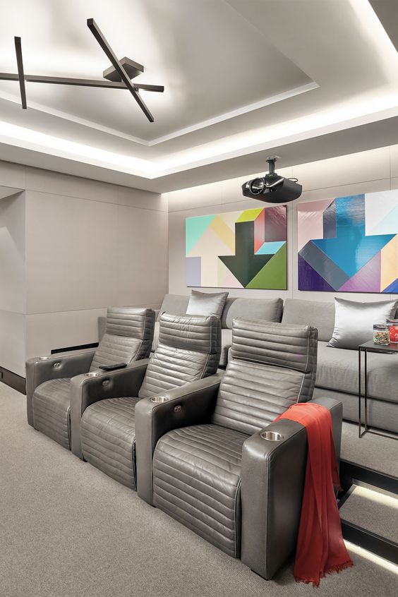 a modern home theater in greys, with grey seating furniture, colorful geometric artwork and built-in lights is a cool space