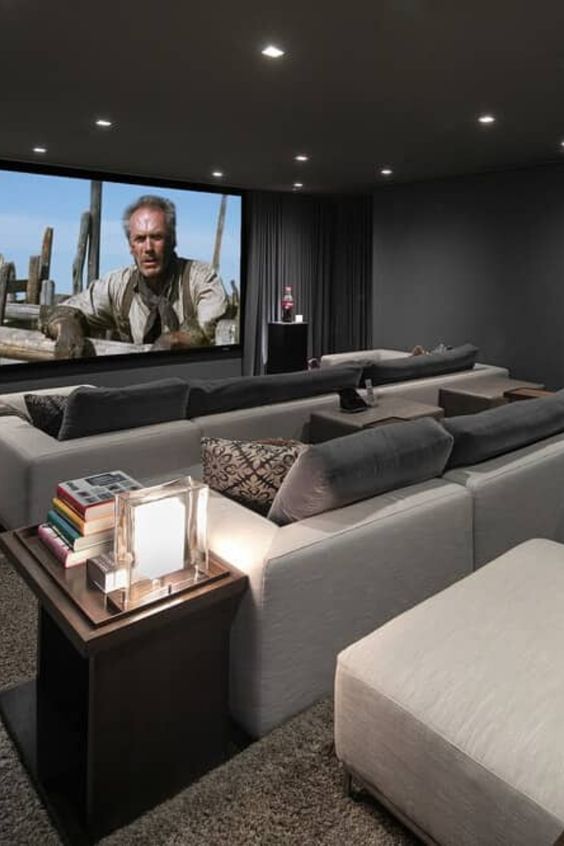 a modern home theater with graphite grey walls, neutral sofas and grey pillows, a large screen, built-in lights and a side table