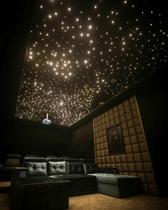 a moody and beautiful home theater with a starry sky ceiling, dark green seating furniture, an upholstered wall and an artwork
