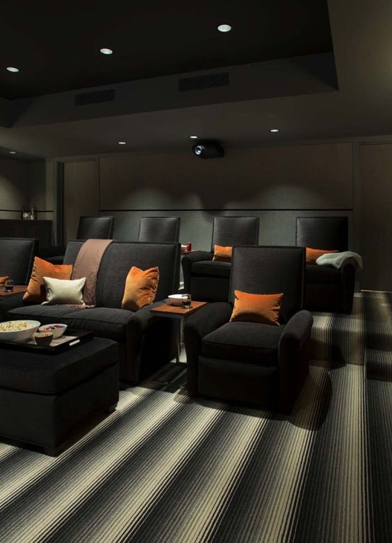 a moody home theater with graphite grey walls and a ceiling with built-in lights, black chairs and sofas, bright pillows