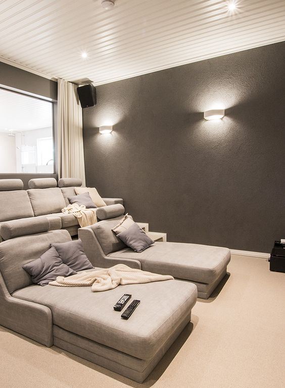 a neutral and comfortable home theater with grey seating furniture, grey walls, neutral textiles and elegant sconces and built-in lights