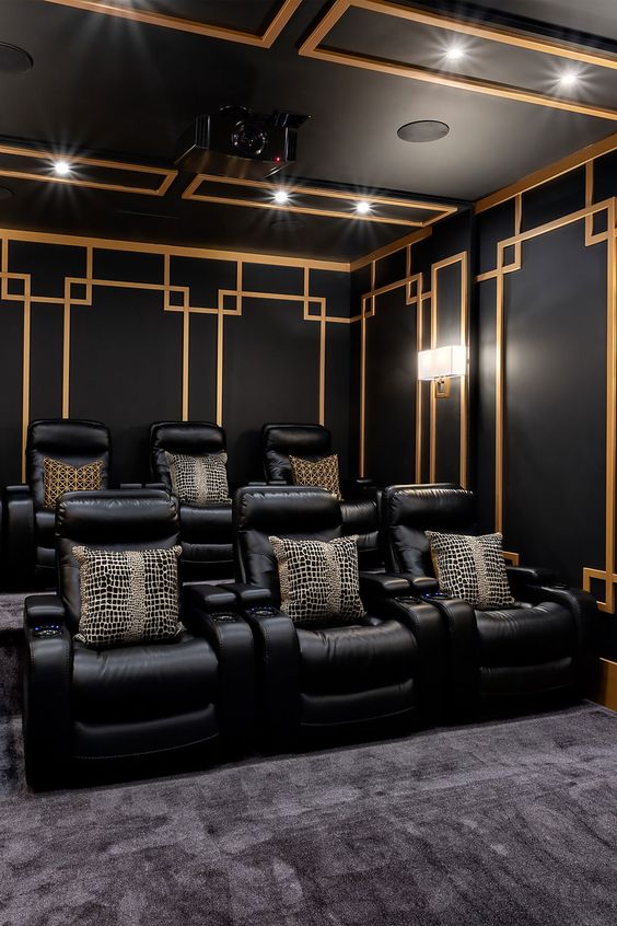 a pretty art deco inspired home theater with black and gold walls, black leather chairs and printed pillows is a stylish and chic space