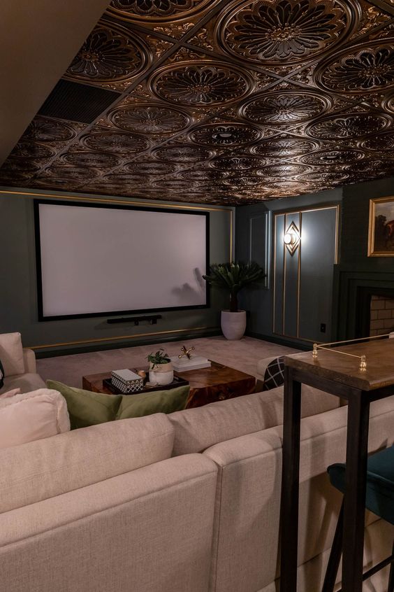 a refined home theater with grey and gold walls, a beautiful ceiling, neutral seating furniture, a stained console table and a large screen